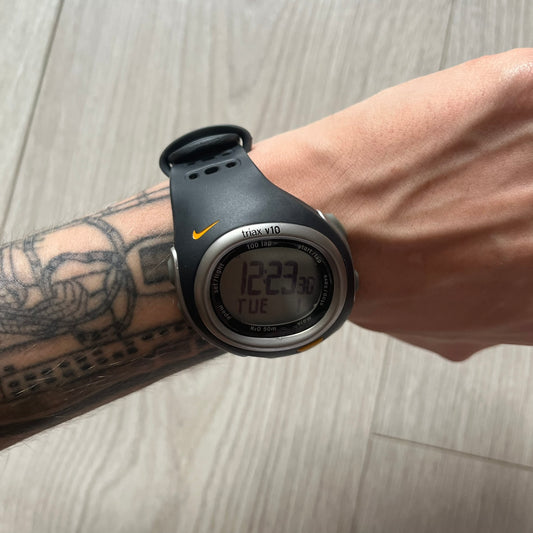 Black digital watch on a wrist with a tattoo, on a light wooden surface