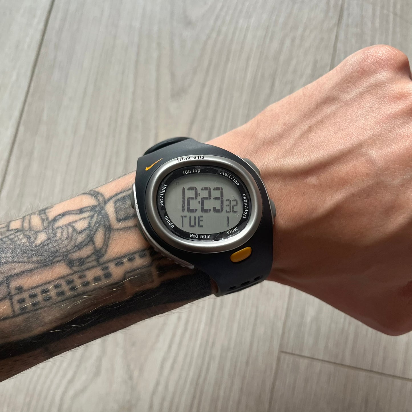 Digital watch on a wrist with tattoos against a wooden background