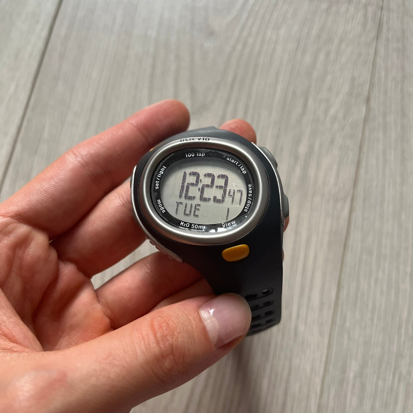 Digital watch held in a hand against a wooden surface