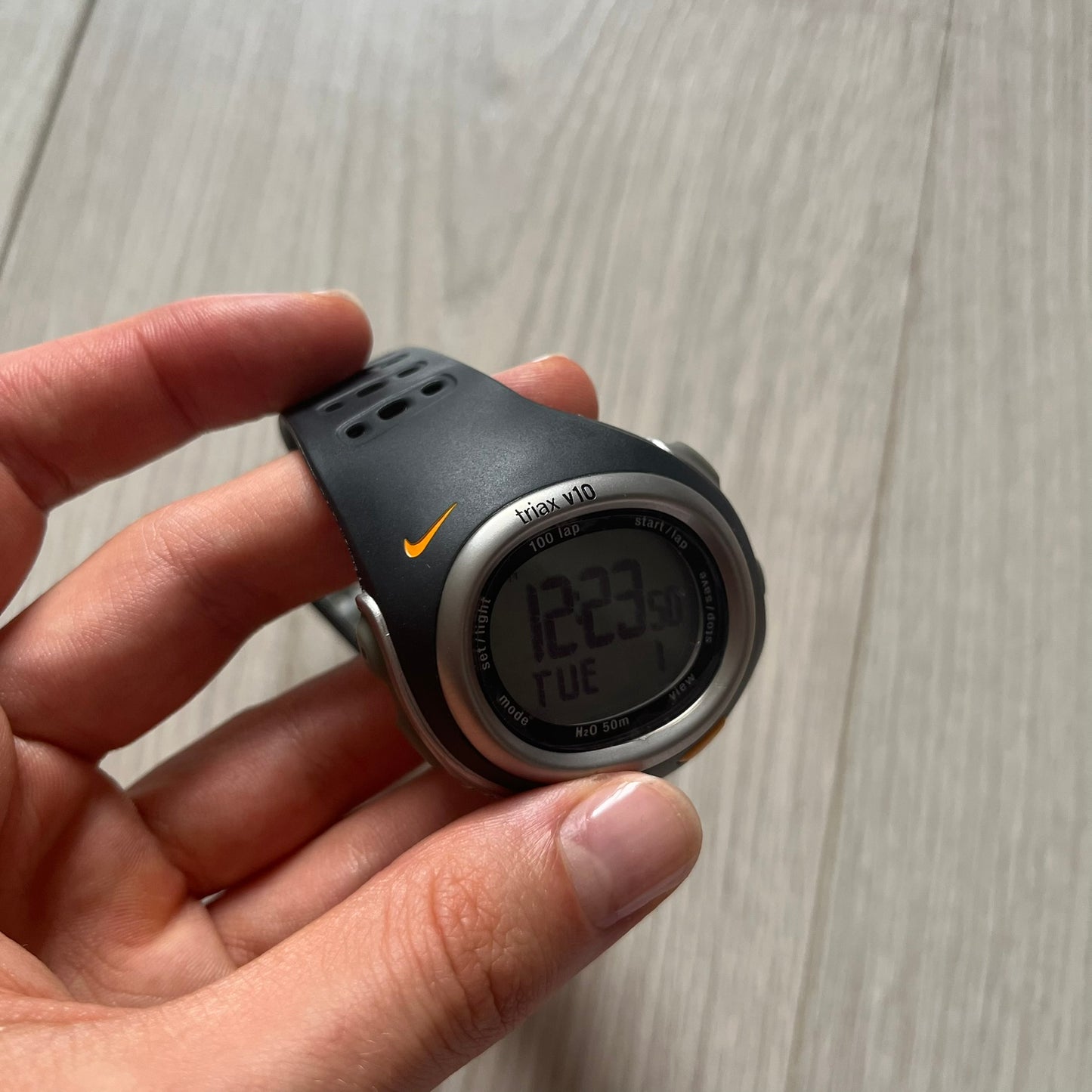 Hand holding a digital watch with a visible Nike logo on a wooden surface