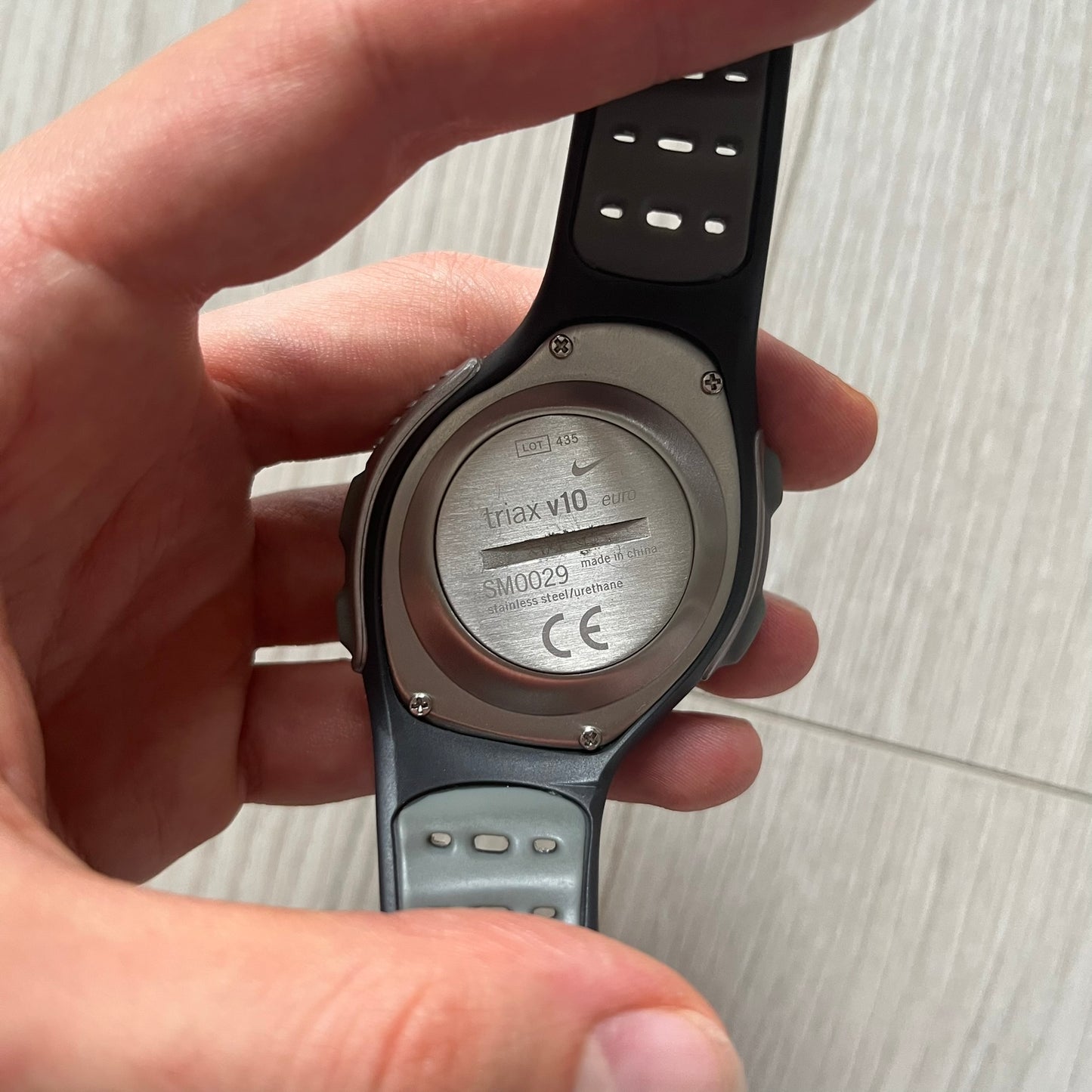 Hand holding a smartwatch with a visible backside label on a light background