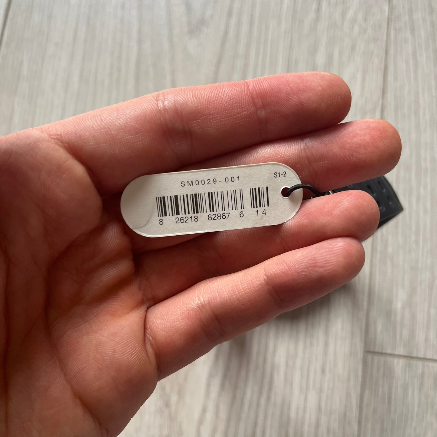 Hand holding a metal tag with a barcode on a light wooden surface