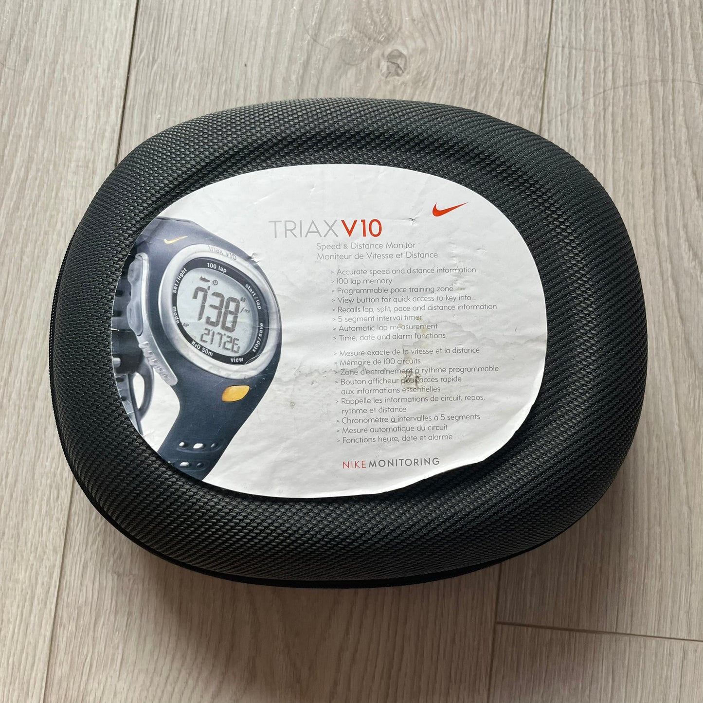 Black mesh container with Triax V10 device packaging on a wooden floor