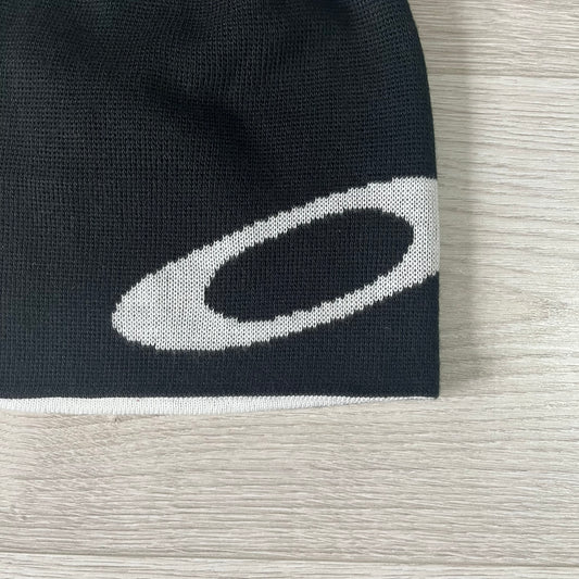 Black knit beanie with a white logo on a light wooden surface