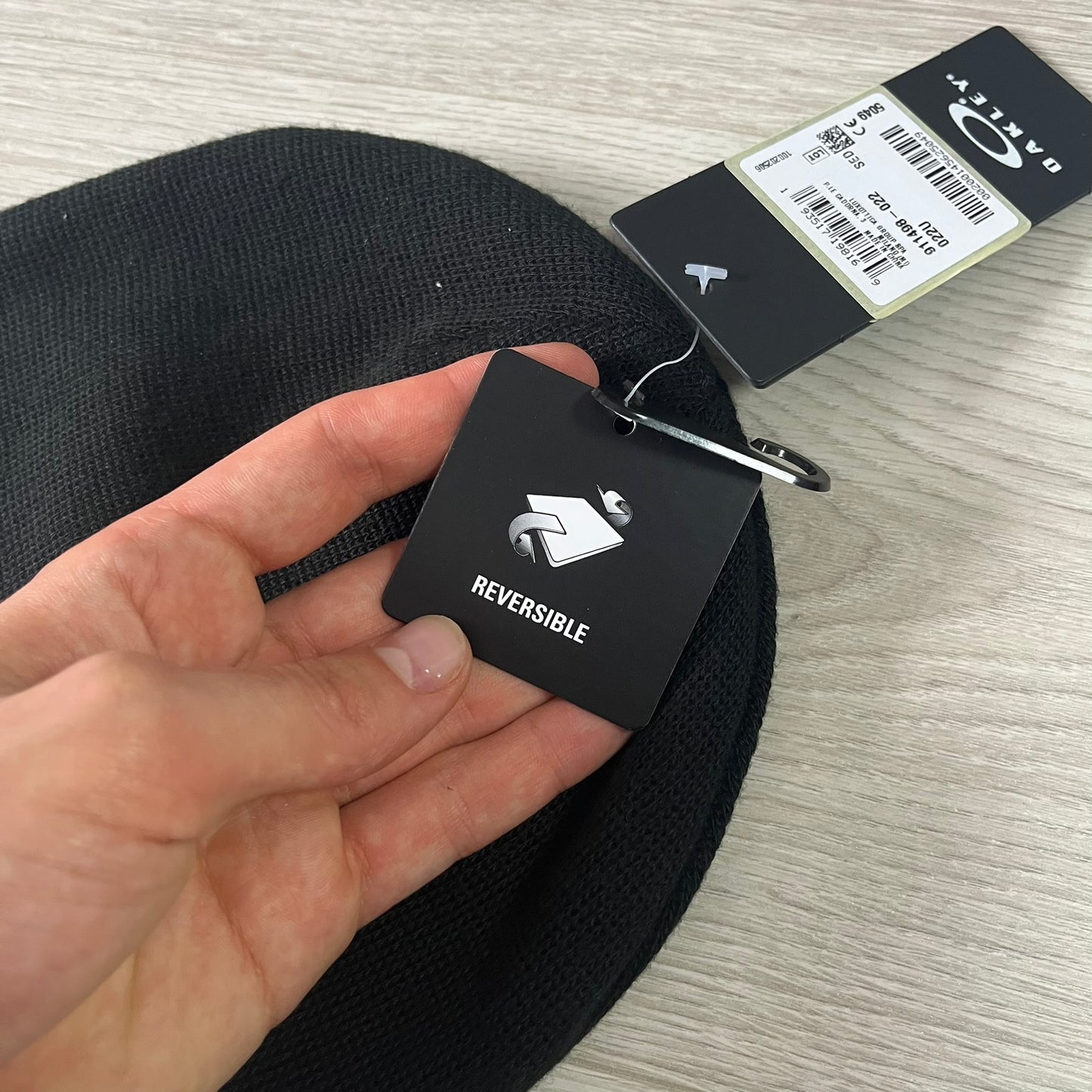 Black reversible belt with a brand tag held by a hand on a light gray surface