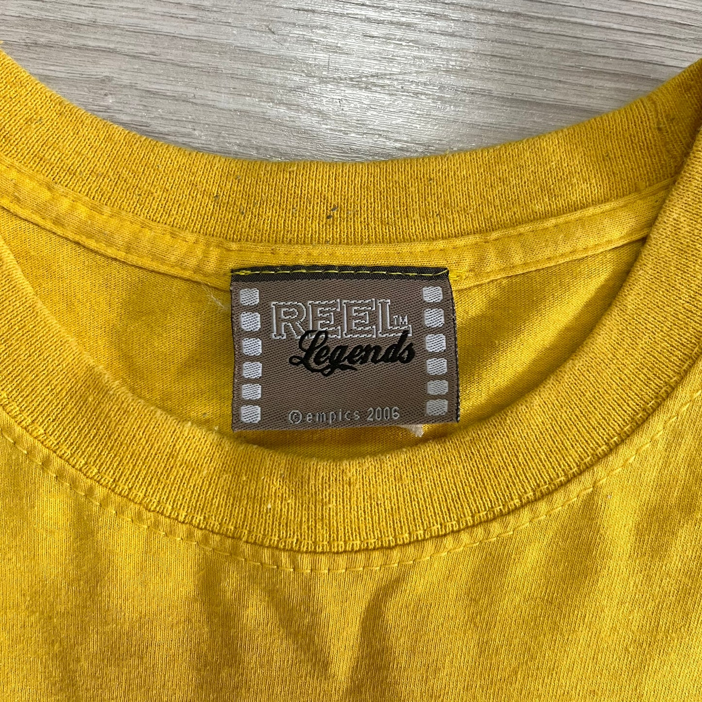 Close-up of a yellow shirt with a 'Reel Legends' label on a gray background