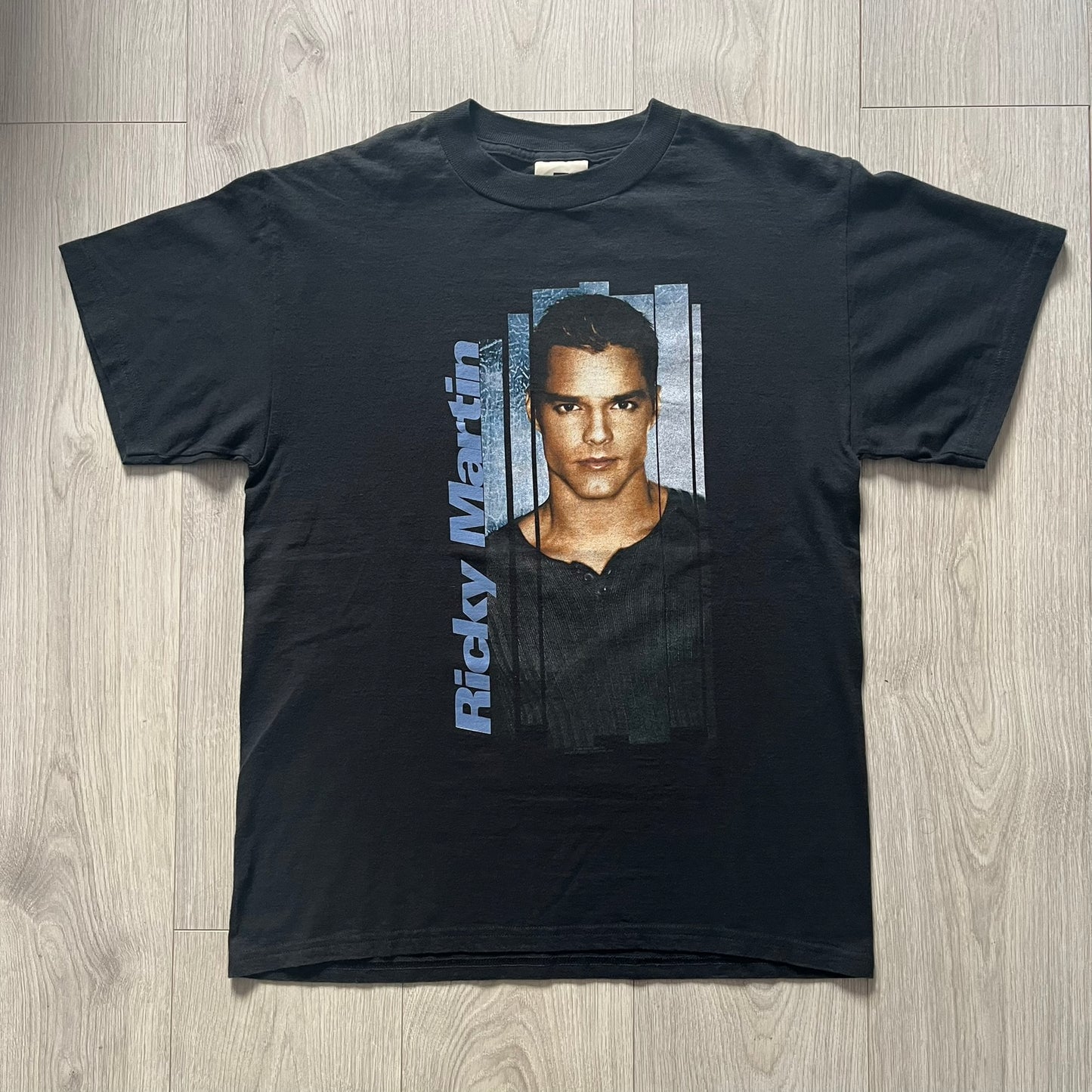 Black t-shirt with a graphic of a person and 'Ricky Martin' text on a wooden surface