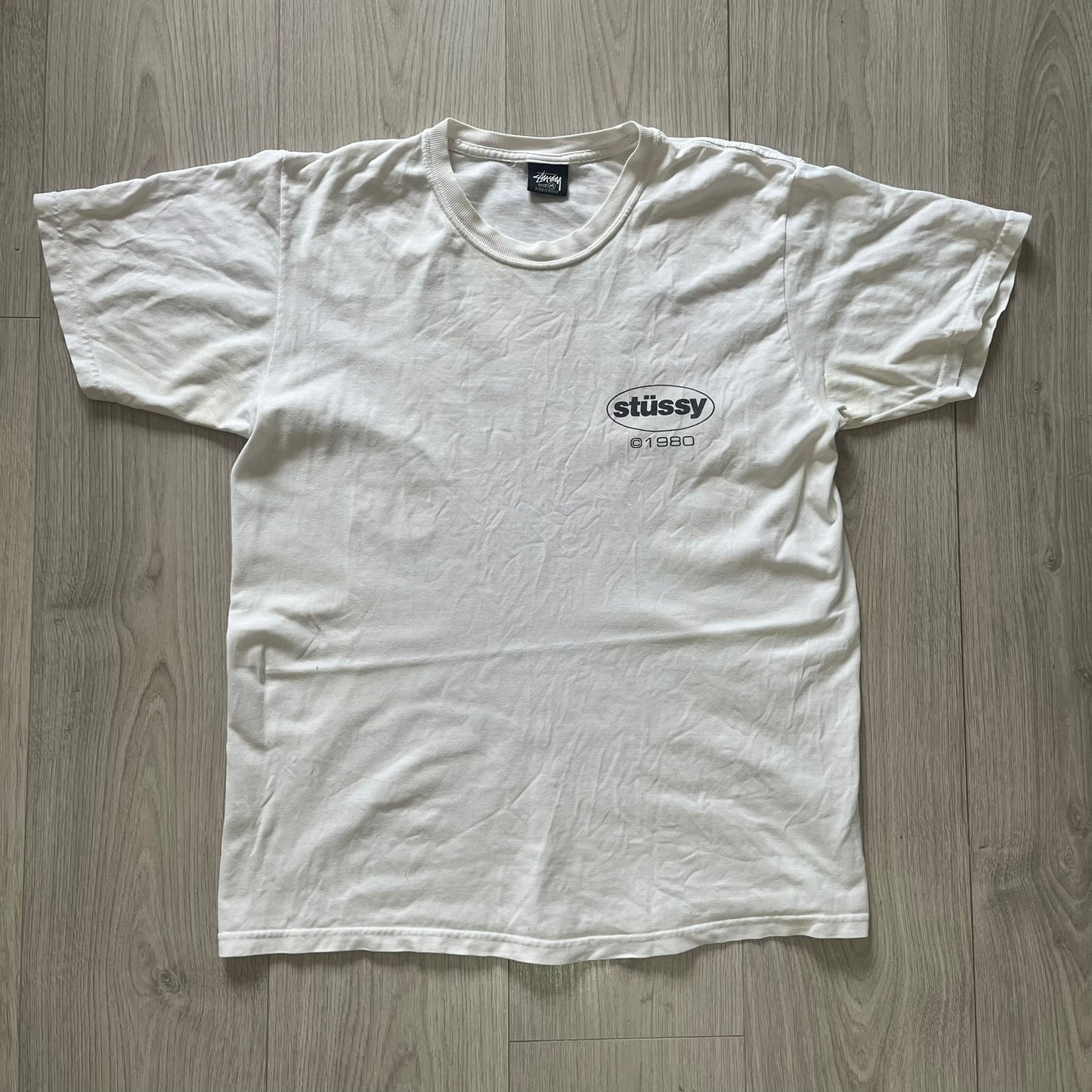 White t-shirt with Stussy logo on a wooden surface