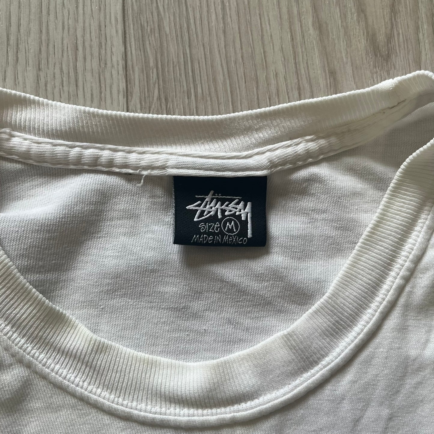 White t-shirt with a Stussy label on a wooden surface
