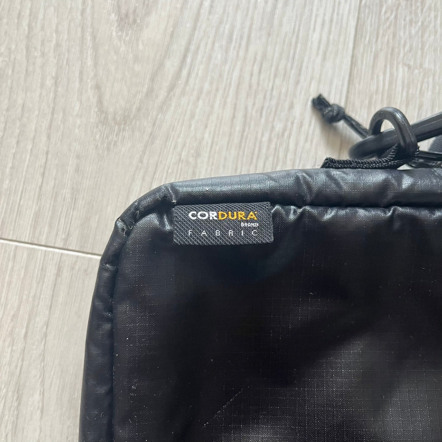Black bag with a Cordura fabric label on a wooden floor.