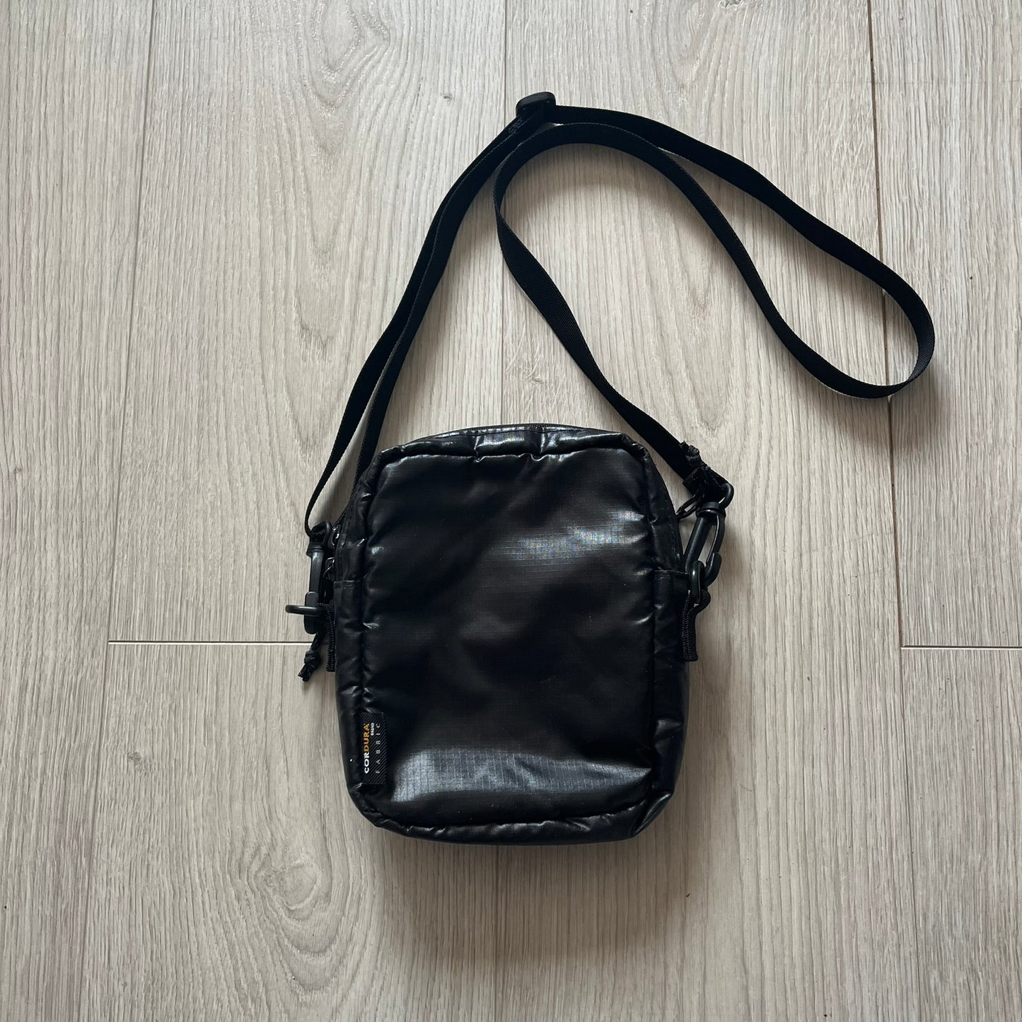 Black leather crossbody bag on a light wood floor