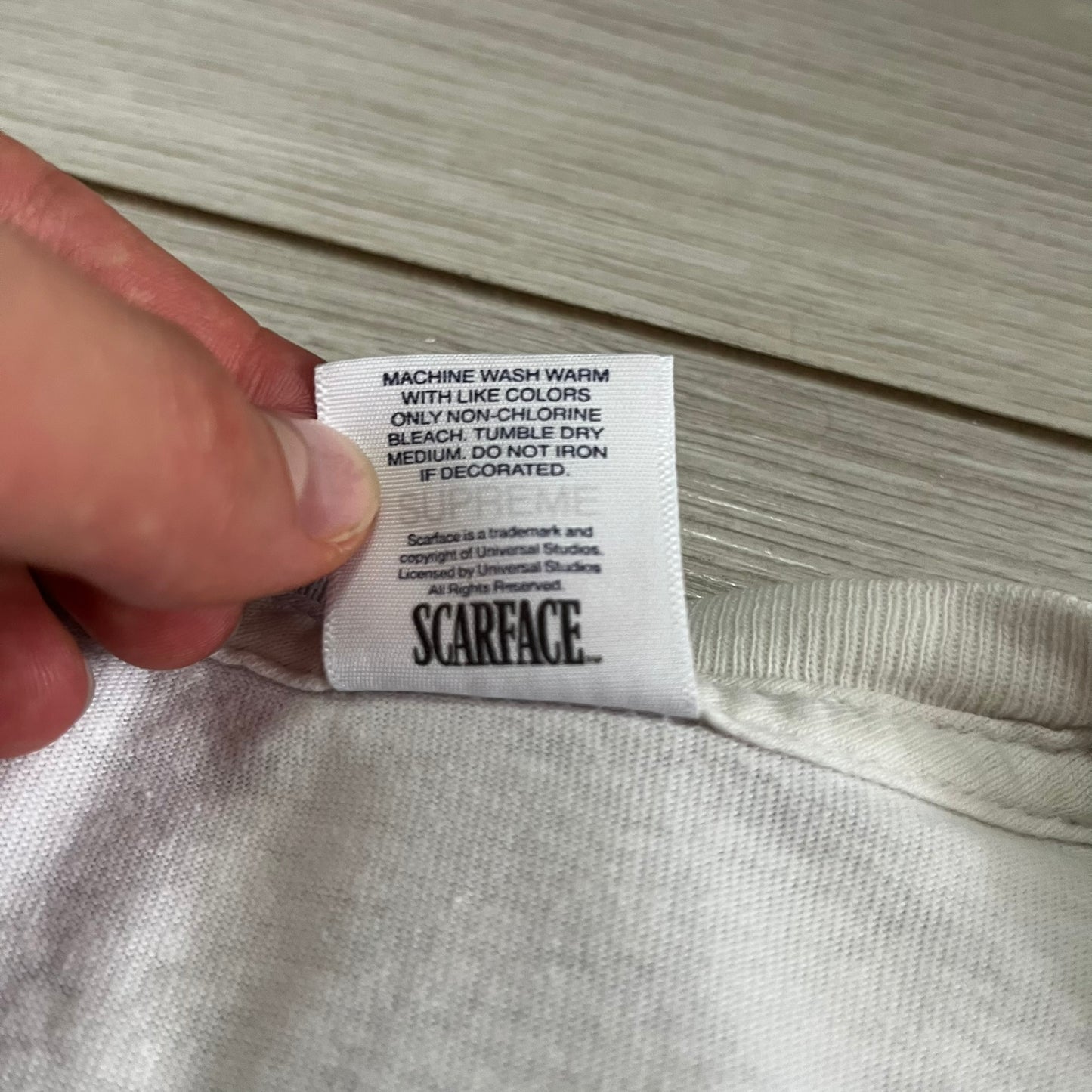 Close-up of a 'Scarface' label on a garment with a hand holding it.