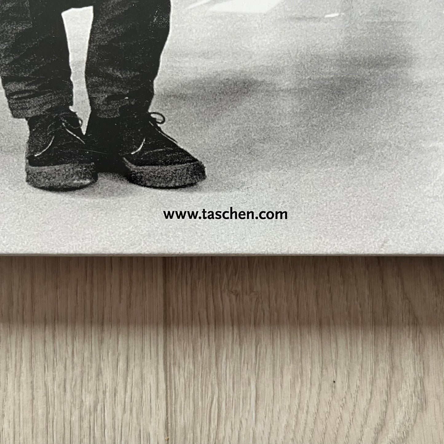 Black and white photo of a person's feet wearing shoes on a reflective surface, with 'www.taschen.com' text.