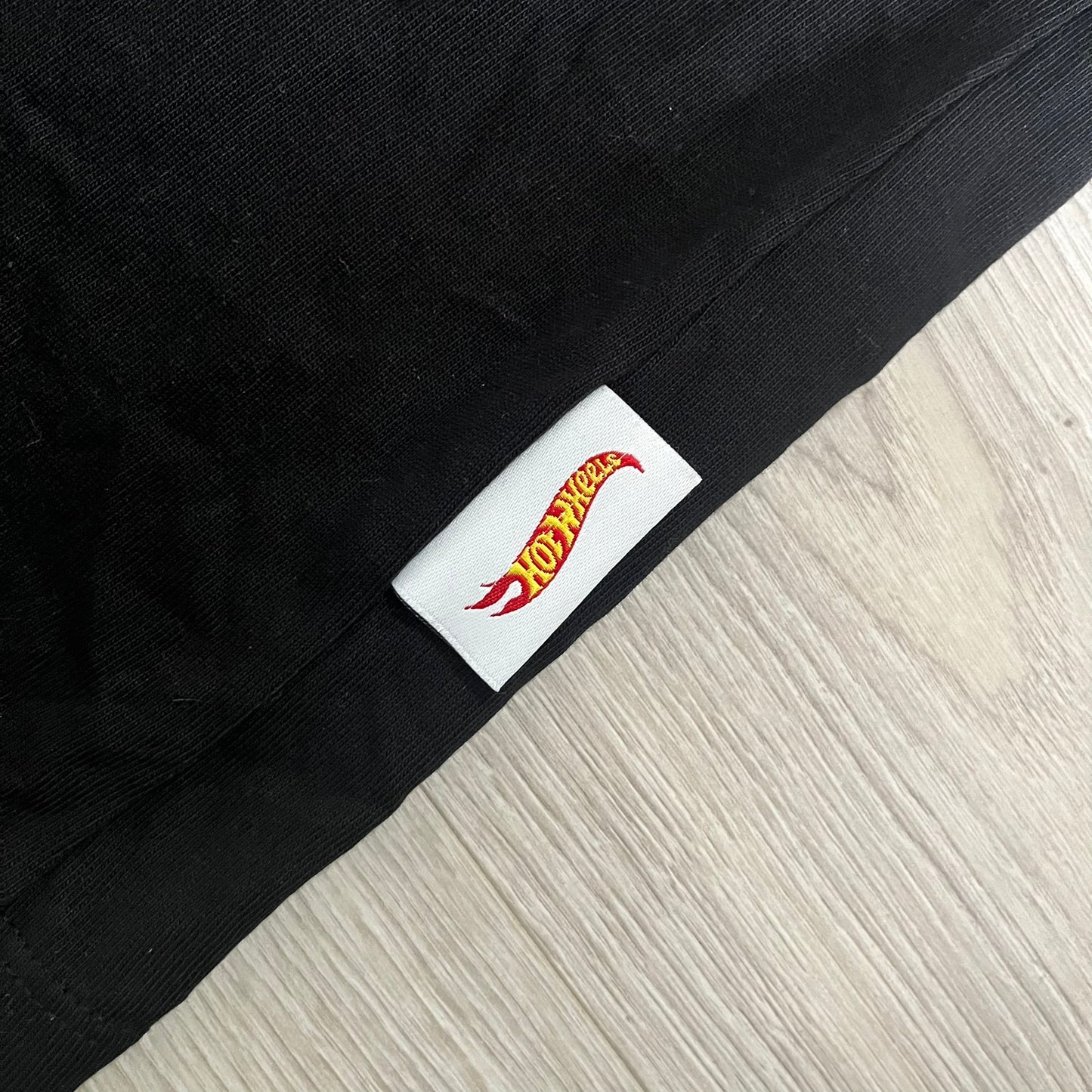 Black fabric with a Hot Wheels logo tag on a light wood floor.