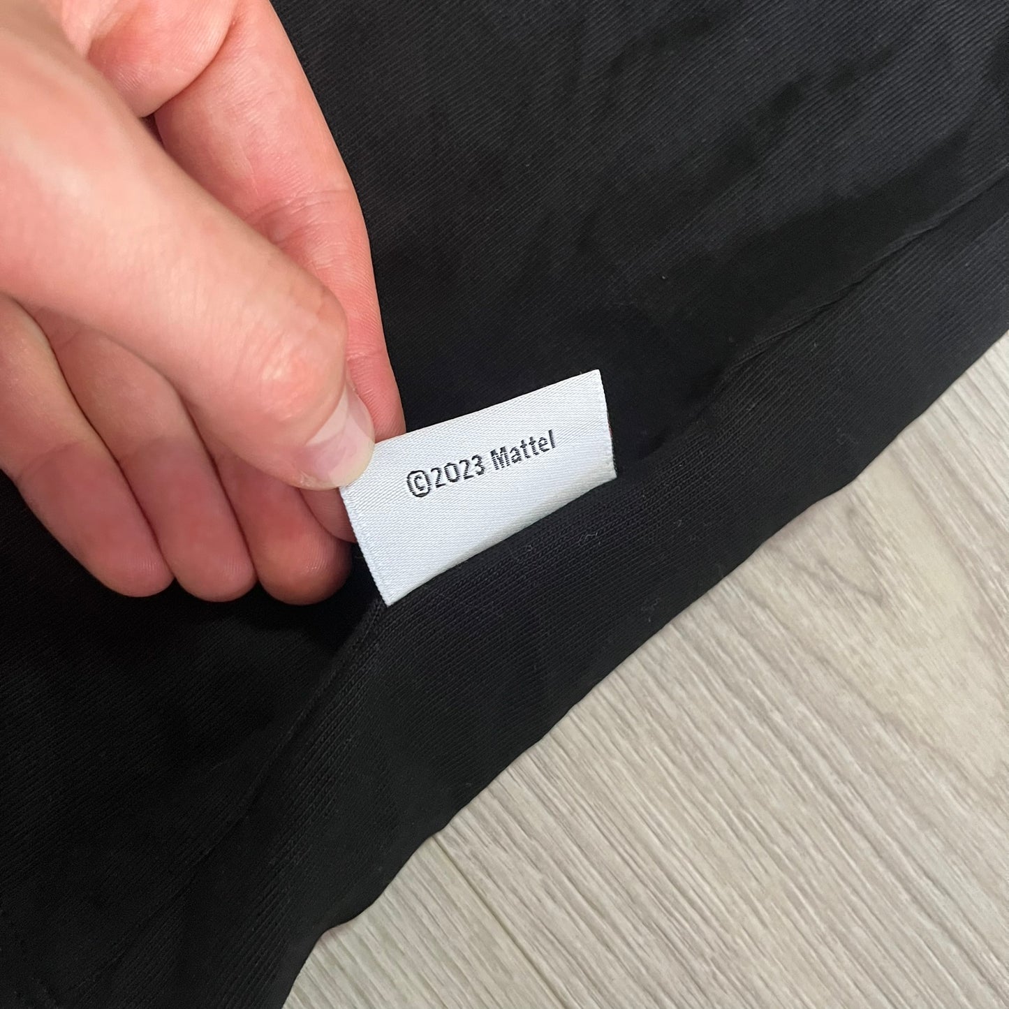 Hand holding a label on black fabric with '©2023 Mattel' text.