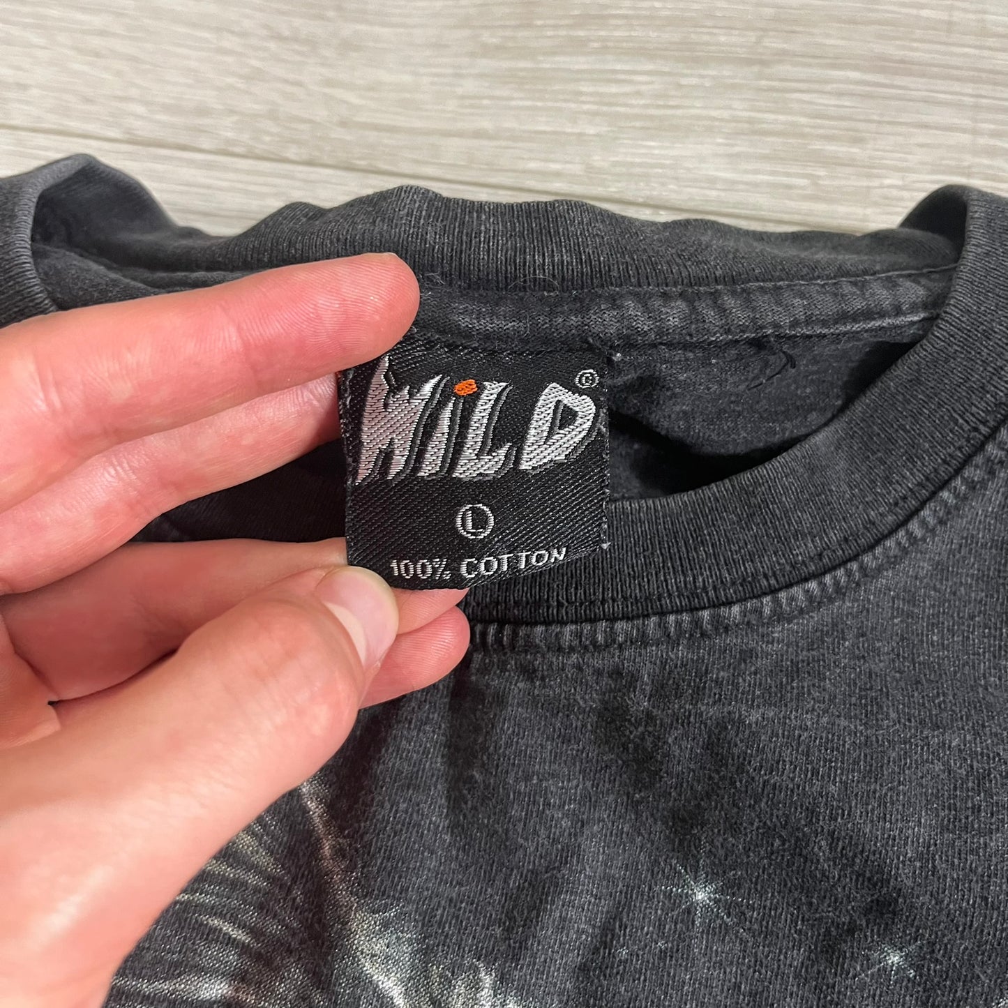 Hand holding a label on a gray shirt with 'WILD' branding.