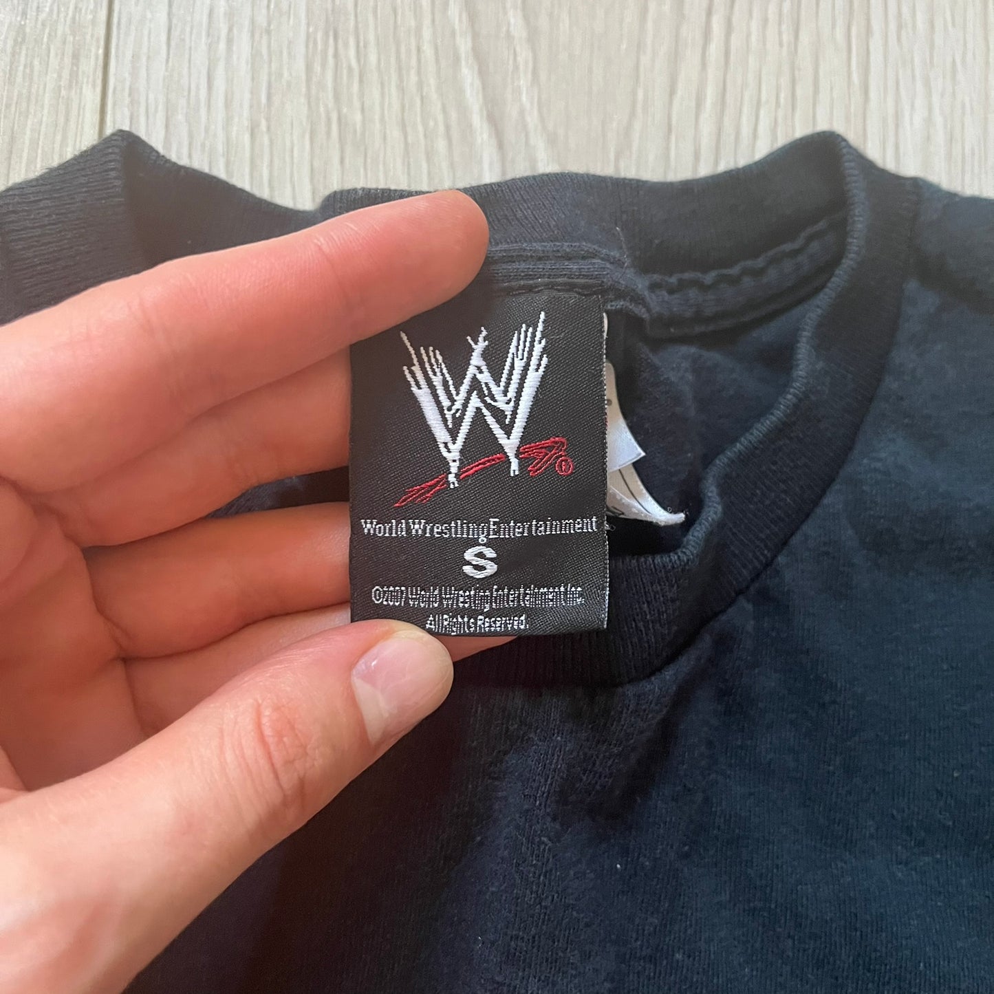 Hand holding a World Wrestling Entertainment tag on a dark blue garment.
