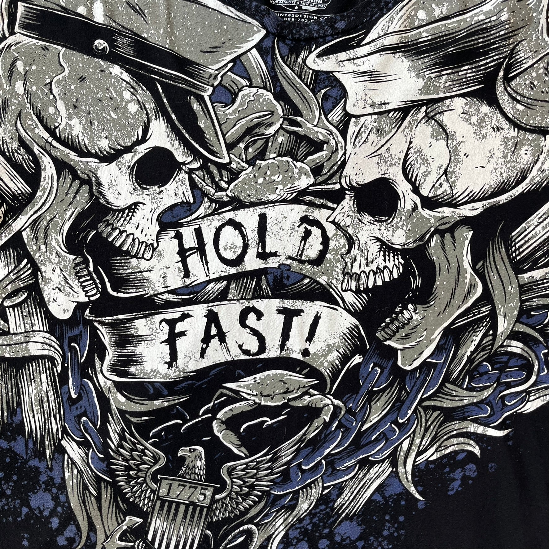 7.62 Design US Navy Black Tee features large front and back graphics in black, white, grey, and navy. The front has two skulls, bones, and US Navy graphics covering most of the shirt. The back has a smaller US Navy logo graphic.
