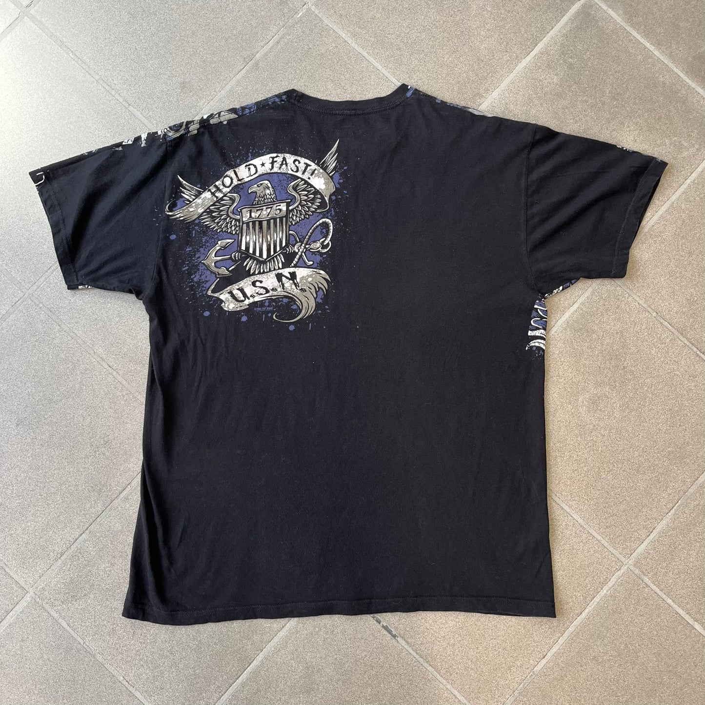 7.62 Design US Navy Black Tee features large front and back graphics in black, white, grey, and navy. The front has two skulls, bones, and US Navy graphics covering most of the shirt. The back has a smaller US Navy logo graphic.
