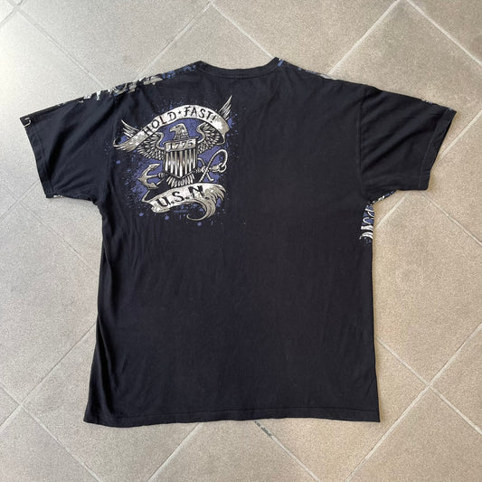 7.62 Design US Navy Black Tee features large front and back graphics in black, white, grey, and navy. The front has two skulls, bones, and US Navy graphics covering most of the shirt. The back has a smaller US Navy logo graphic.
