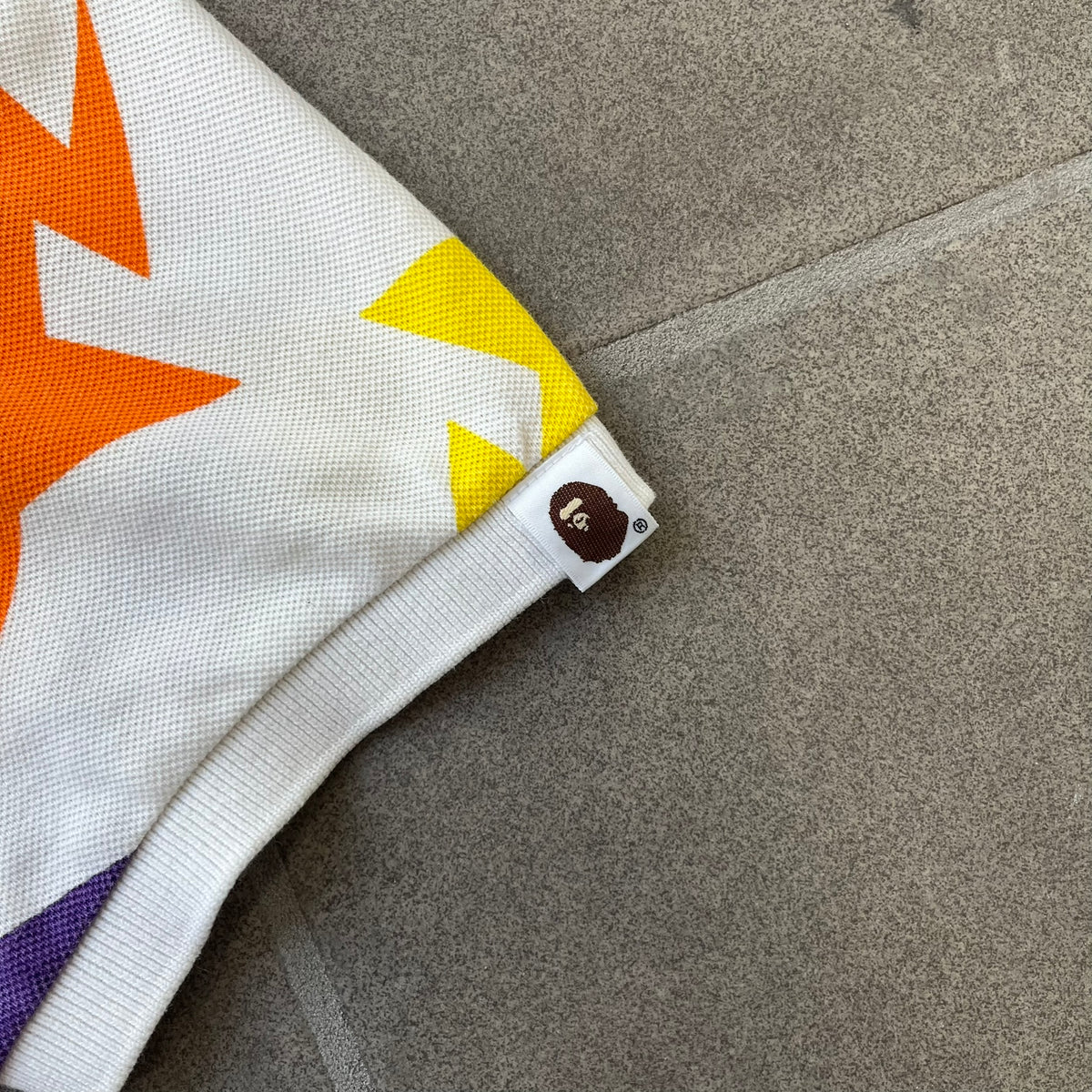 A Bathing Ape 2014 Milo Multicolor Sta Polo is a white, 100% cotton BAPE polo featuring an all-over print of multicolor STA (shooting star) graphics in pink, green, blue, yellow, red (and more), some featuring eyes. It includes branded Bape buttons.
