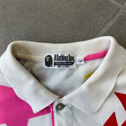 A Bathing Ape 2014 Milo Multicolor Sta Polo is a white, 100% cotton BAPE polo featuring an all-over print of multicolor STA (shooting star) graphics in pink, green, blue, yellow, red (and more), some featuring eyes. It includes branded Bape buttons.