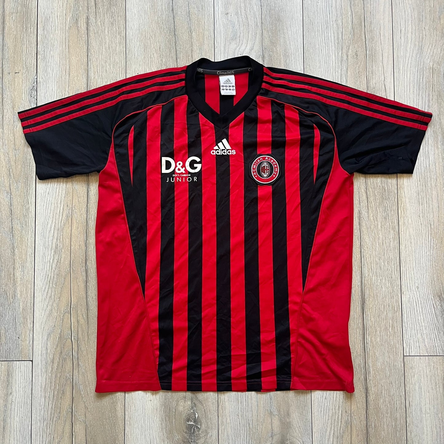AC Milan Academy x Dolce &amp; Gabbana 2008/09 Home Tee is a black and red striped football shirt with black short sleeves. The chest features AC Milan Academy and Dolce &amp; Gabbana Junior logos on the sides, and a adidas logo in the center. Made with Clima365 technology.

