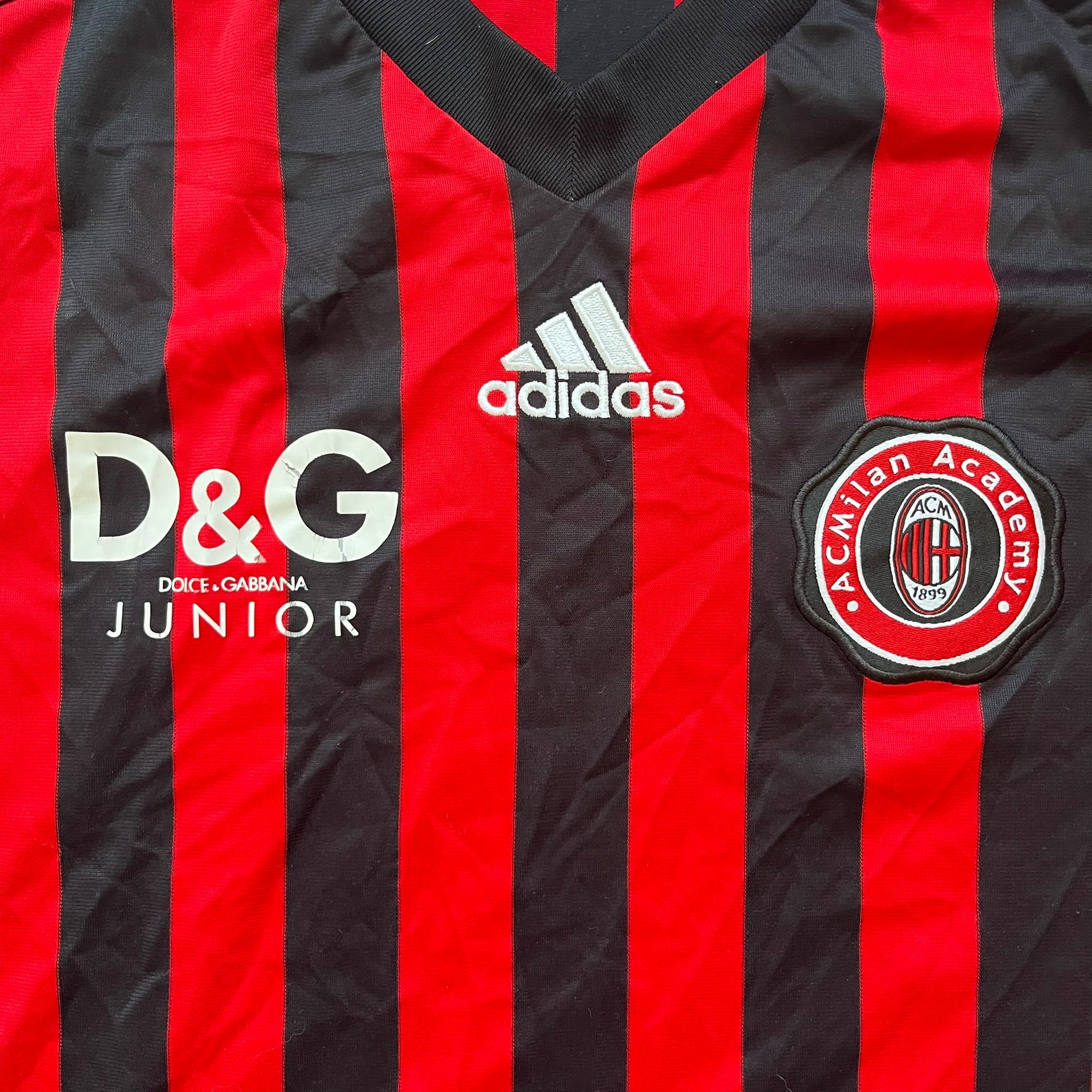 AC Milan Academy x Dolce &amp; Gabbana 2008/09 Home Tee is a black and red striped football shirt with black short sleeves. The chest features AC Milan Academy and Dolce &amp; Gabbana Junior logos on the sides, and a adidas logo in the center. Made with Clima365 technology.
