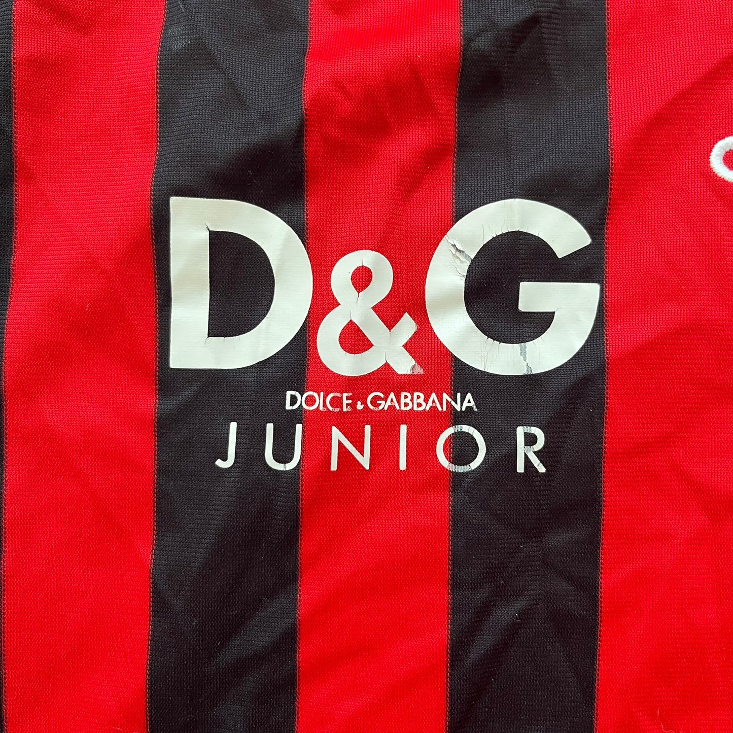 AC Milan Academy x Dolce &amp; Gabbana 2008/09 Home Tee is a black and red striped football shirt with black short sleeves. The chest features AC Milan Academy and Dolce &amp; Gabbana Junior logos on the sides, and a adidas logo in the center. Made with Clima365 technology.
