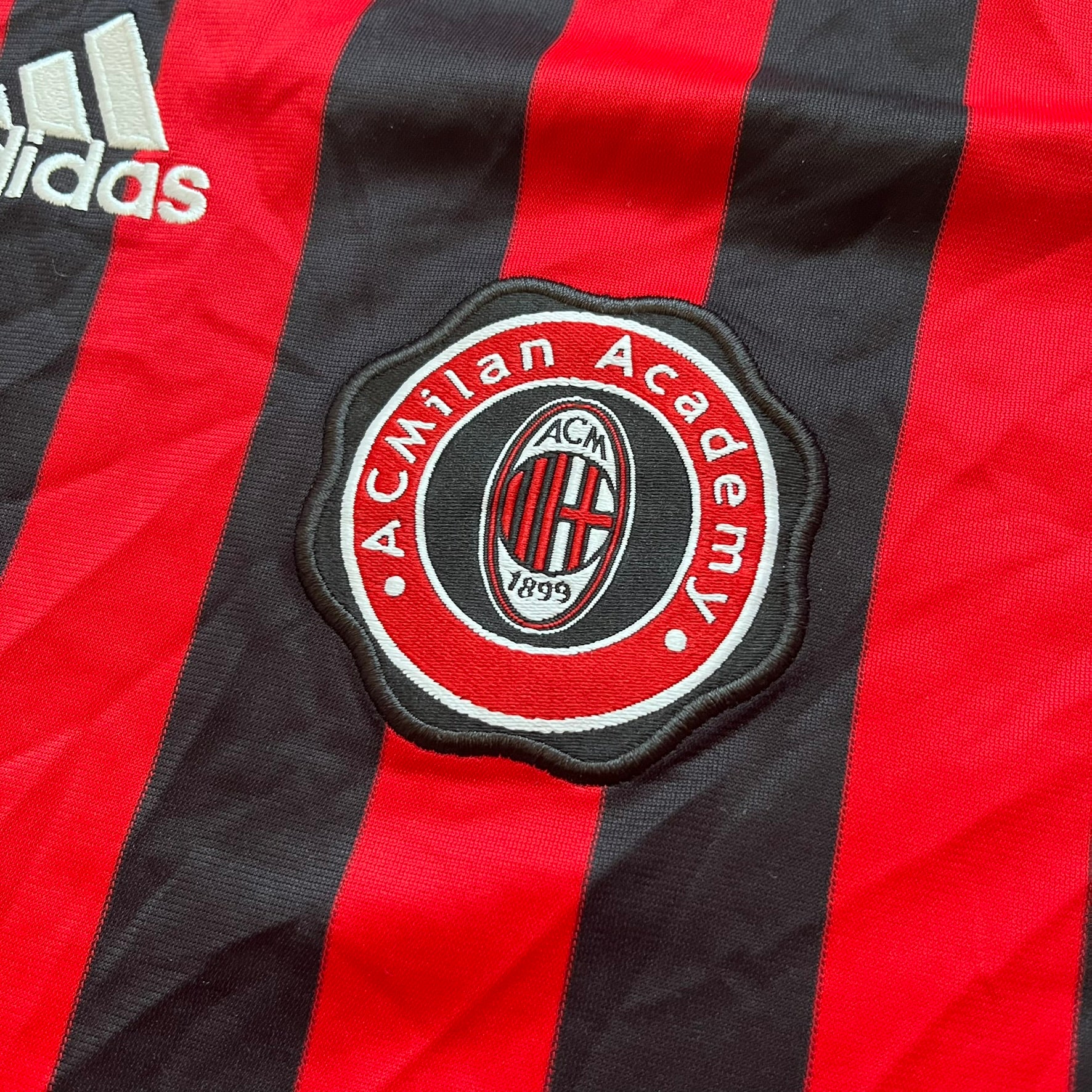 AC Milan Academy x Dolce &amp; Gabbana 2008/09 Home Tee is a black and red striped football shirt with black short sleeves. The chest features AC Milan Academy and Dolce &amp; Gabbana Junior logos on the sides, and a adidas logo in the center. Made with Clima365 technology.
