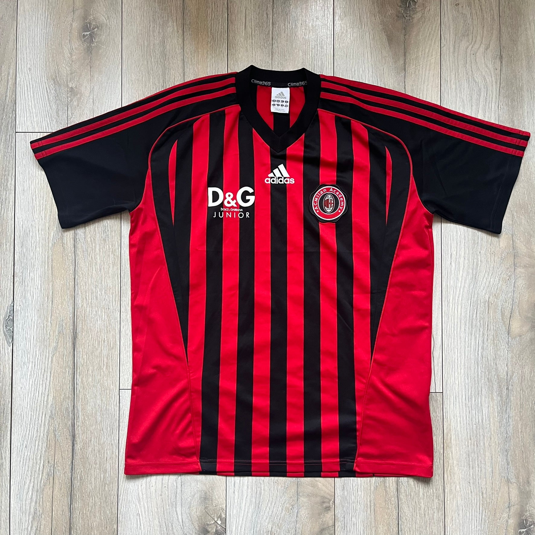 AC Milan Academy x Dolce &amp; Gabbana 2008/09 Home Tee is a black and red striped football shirt with black short sleeves. The chest features AC Milan Academy and Dolce &amp; Gabbana Junior logos on the sides, and a adidas logo in the center. Made with Clima365 technology.