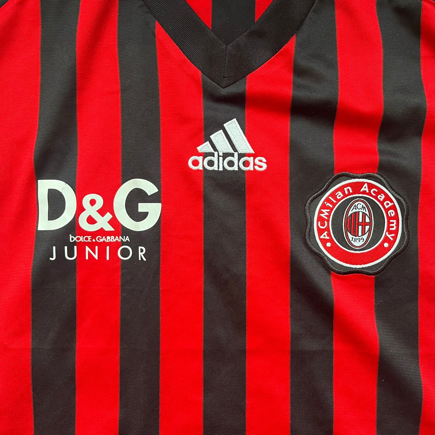 AC Milan Academy x Dolce &amp; Gabbana 2008/09 Home Tee is a black and red striped football shirt with black short sleeves. The chest features AC Milan Academy and Dolce &amp; Gabbana Junior logos on the sides, and a adidas logo in the center. Made with Clima365 technology.