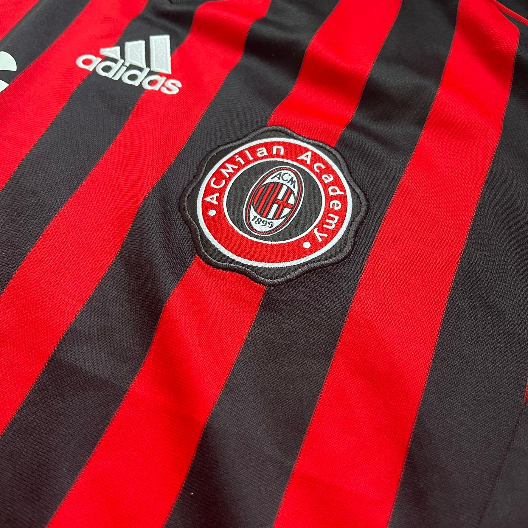 AC Milan Academy x Dolce &amp; Gabbana 2008/09 Home Tee is a black and red striped football shirt with black short sleeves. The chest features AC Milan Academy and Dolce &amp; Gabbana Junior logos on the sides, and a adidas logo in the center. Made with Clima365 technology.