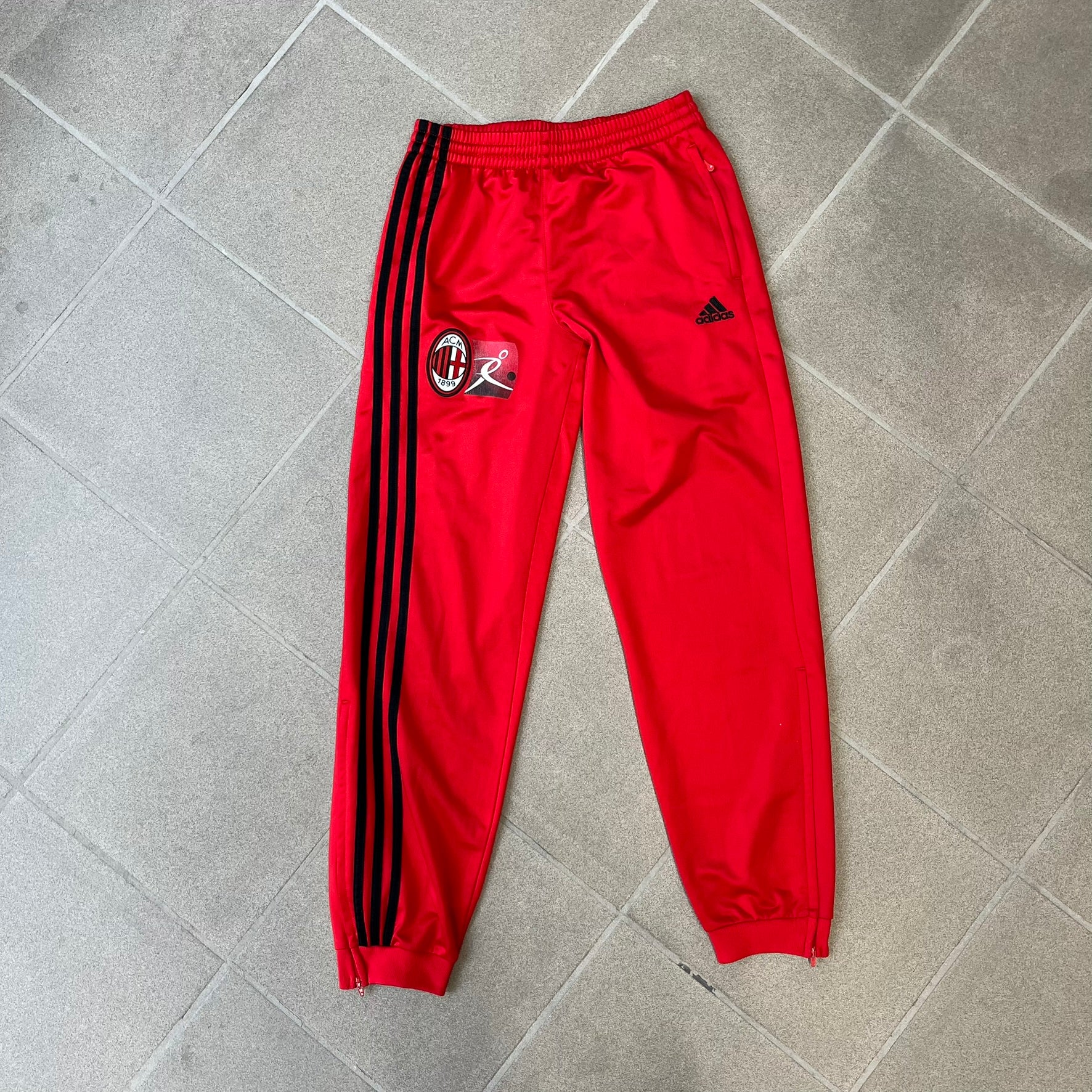 AC Milan x Adidas 2009/10 Junior Track Pants are a black and red junior football track bottoms with 3 black Adidas lines on the side. The right leg features AC Milan logo patch on one side, and Adidas logo embroidered on the left. Made with Climacool technology, it is designed for youth performance wear.