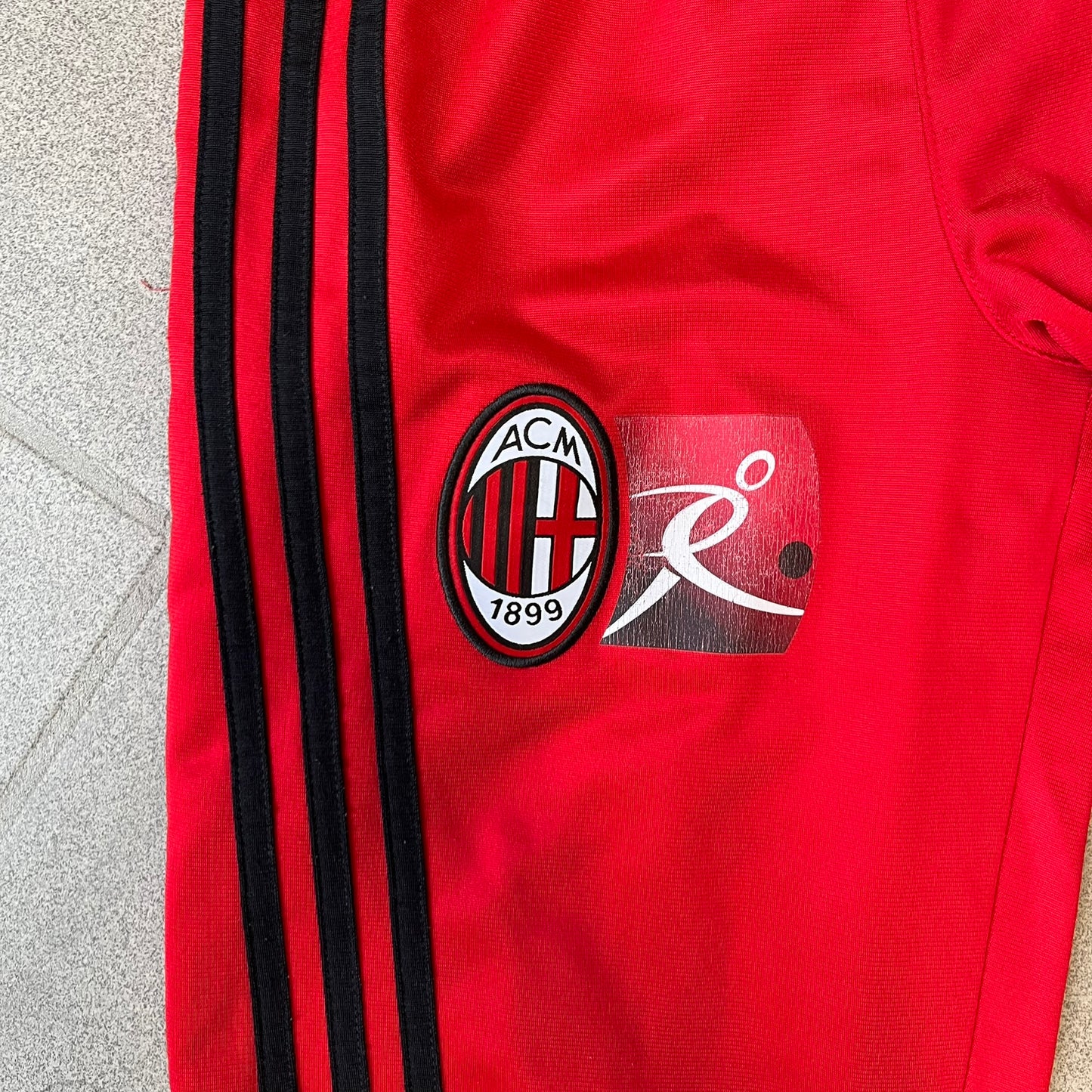 AC Milan x Adidas 2009/10 Junior Track Pants are a black and red junior football track bottoms with 3 black Adidas lines on the side. The right leg features AC Milan logo patch on one side, and Adidas logo embroidered on the left. Made with Climacool technology, it is designed for youth performance wear.