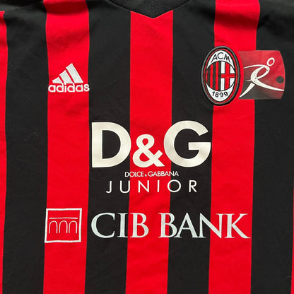 AC Milan x Dolce & Gabbana 2009/10 Home Tee is a black and red striped junior football shirt with black short sleeves. The chest features AC Milan and Adidas logos on the sides, and a D&G Dolce & Gabbana Junior logo in the center. Made with Climacool technology, it is designed for youth performance wear.