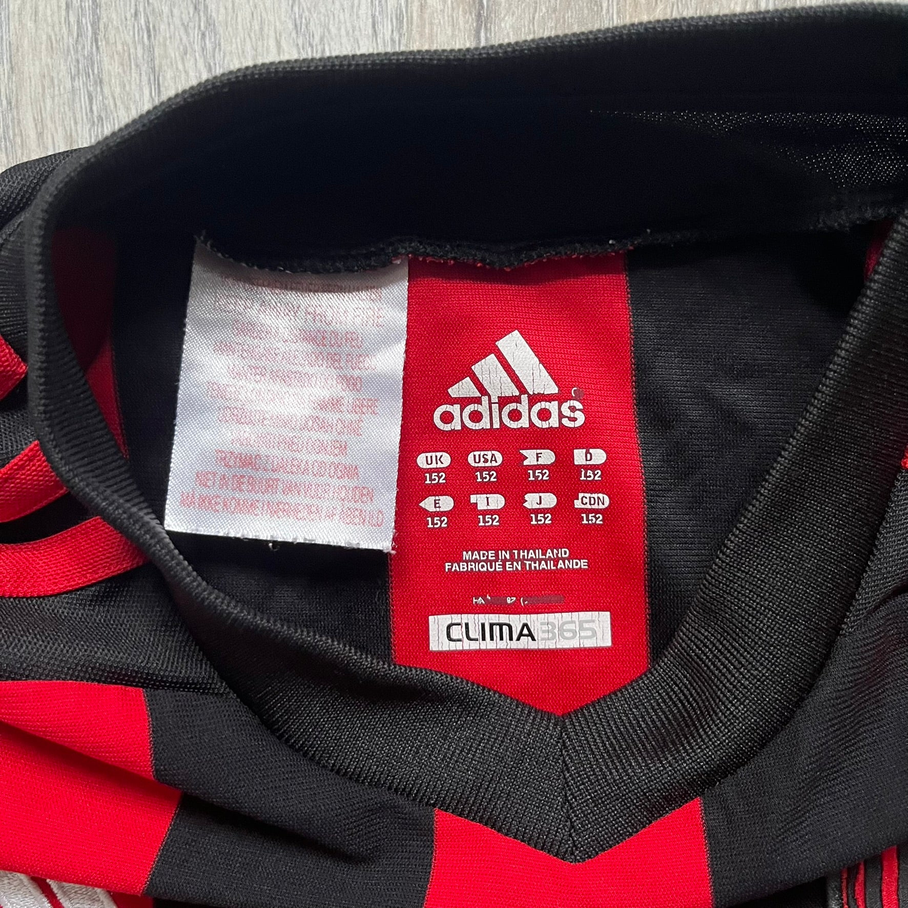 AC Milan x Dolce & Gabbana 2009/10 Home Tee is a black and red striped junior football shirt with black short sleeves. The chest features AC Milan and Adidas logos on the sides, and a D&G Dolce & Gabbana Junior logo in the center. Made with Climacool technology, it is designed for youth performance wear.