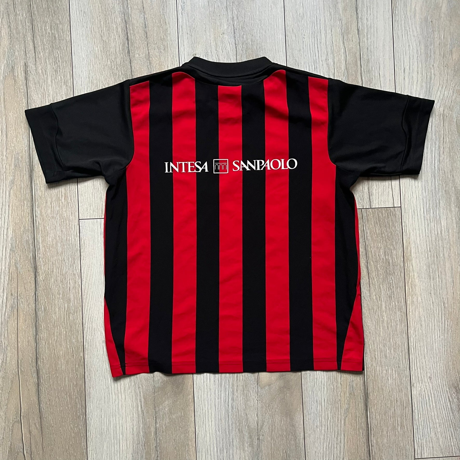 AC Milan x Dolce & Gabbana 2009/10 Home Tee is a black and red striped junior football shirt with black short sleeves. The chest features AC Milan and Adidas logos on the sides, and a D&G Dolce & Gabbana Junior logo in the center. Made with Climacool technology, it is designed for youth performance wear.