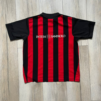AC Milan x Dolce & Gabbana 2009/10 Home Tee is a black and red striped junior football shirt with black short sleeves. The chest features AC Milan and Adidas logos on the sides, and a D&G Dolce & Gabbana Junior logo in the center. Made with Climacool technology, it is designed for youth performance wear.
