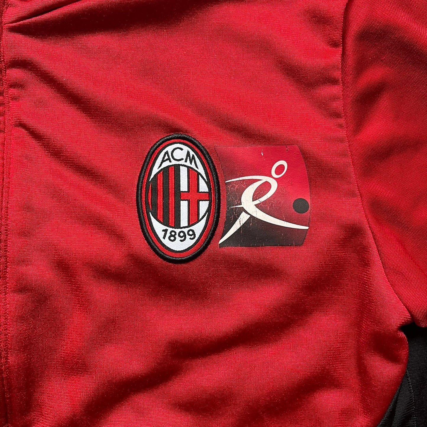 AC Milan x Dolce &amp; Gabbana 2009/10 Track Jacket is a black and red junior football track jacket with asymetrical black and red pattern. The chest features AC Milan and Adidas logos on one side, and a D&amp;G Dolce &amp; Gabbana Junior logo on the left. Made with Climacool technology, it is designed for youth performance wear.