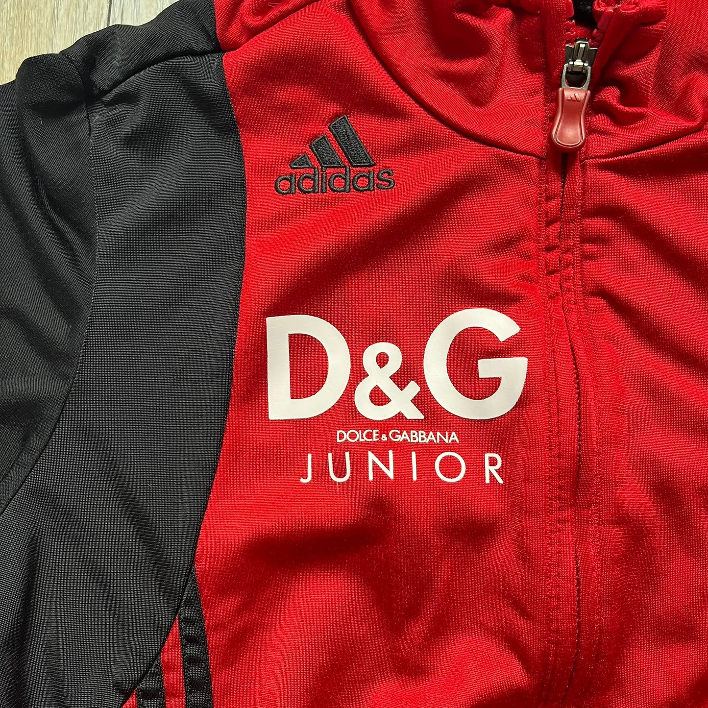 AC Milan x Dolce &amp; Gabbana 2009/10 Track Jacket is a black and red junior football track jacket with asymetrical black and red pattern. The chest features AC Milan and Adidas logos on one side, and a D&amp;G Dolce &amp; Gabbana Junior logo on the left. Made with Climacool technology, it is designed for youth performance wear.