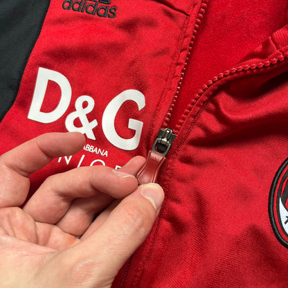 AC Milan x Dolce &amp; Gabbana 2009/10 Track Jacket is a black and red junior football track jacket with asymetrical black and red pattern. The chest features AC Milan and Adidas logos on one side, and a D&amp;G Dolce &amp; Gabbana Junior logo on the left. Made with Climacool technology, it is designed for youth performance wear.