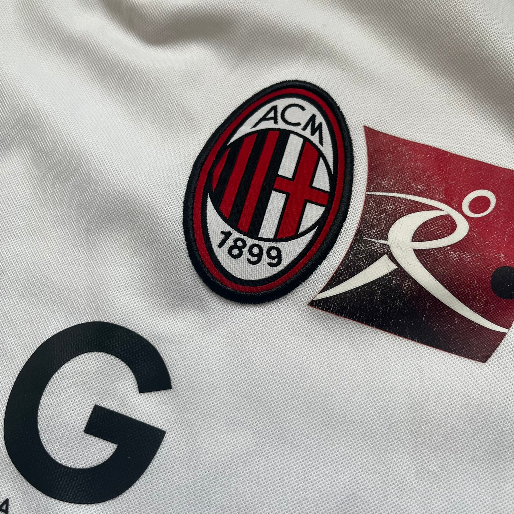 AC Milan x Dolce &amp; Gabbana 2009/10 Training Tee is a white football shirt with red ended short sleeves. The chest features AC Milan and Adidas logos on the sides, and a D&amp;G Dolce &amp; Gabbana Junior logo in the center. Made with Climacool technology, it is designed for performance wear.
