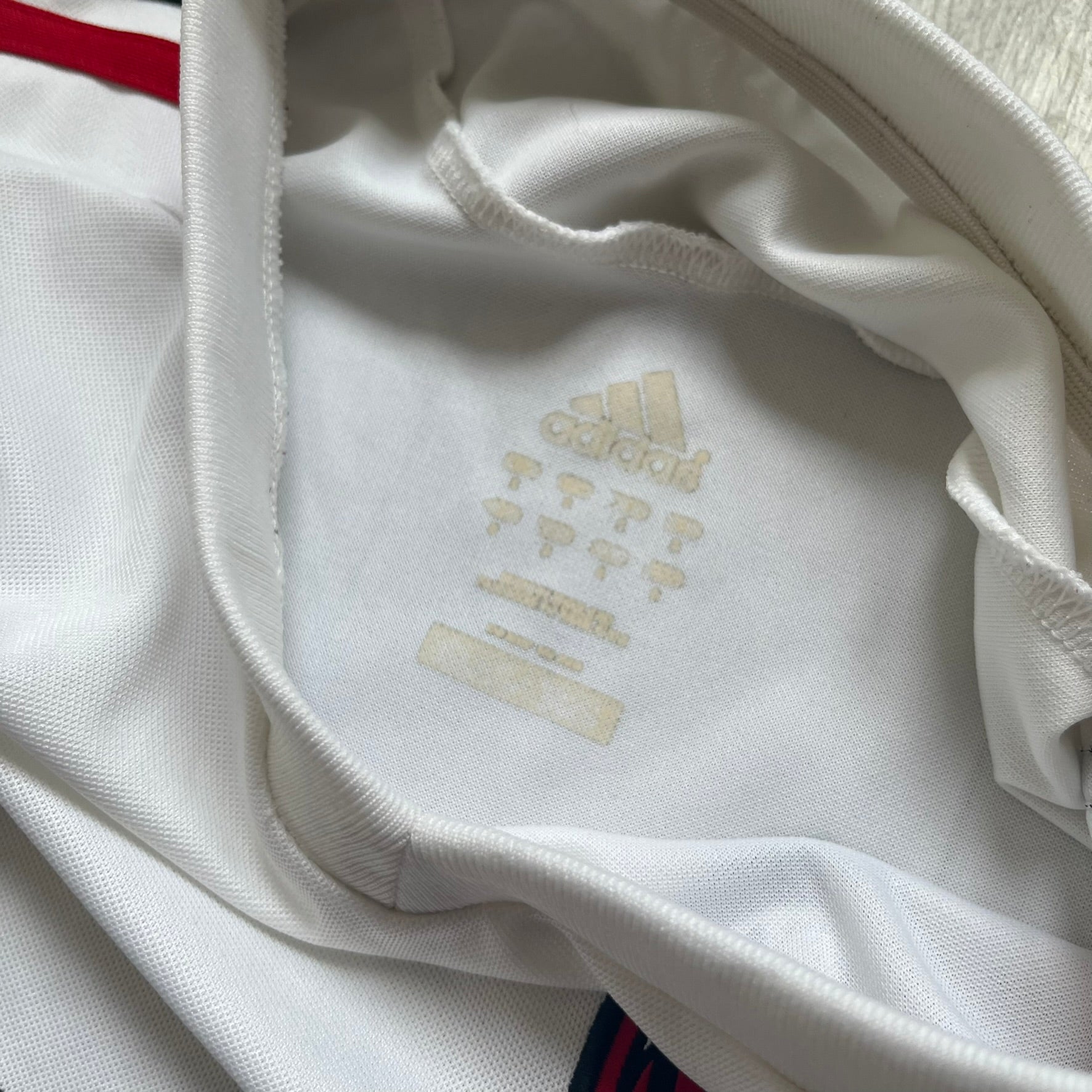 AC Milan x Dolce &amp; Gabbana 2009/10 Training Tee is a white football shirt with red ended short sleeves. The chest features AC Milan and Adidas logos on the sides, and a D&amp;G Dolce &amp; Gabbana Junior logo in the center. Made with Climacool technology, it is designed for performance wear.
