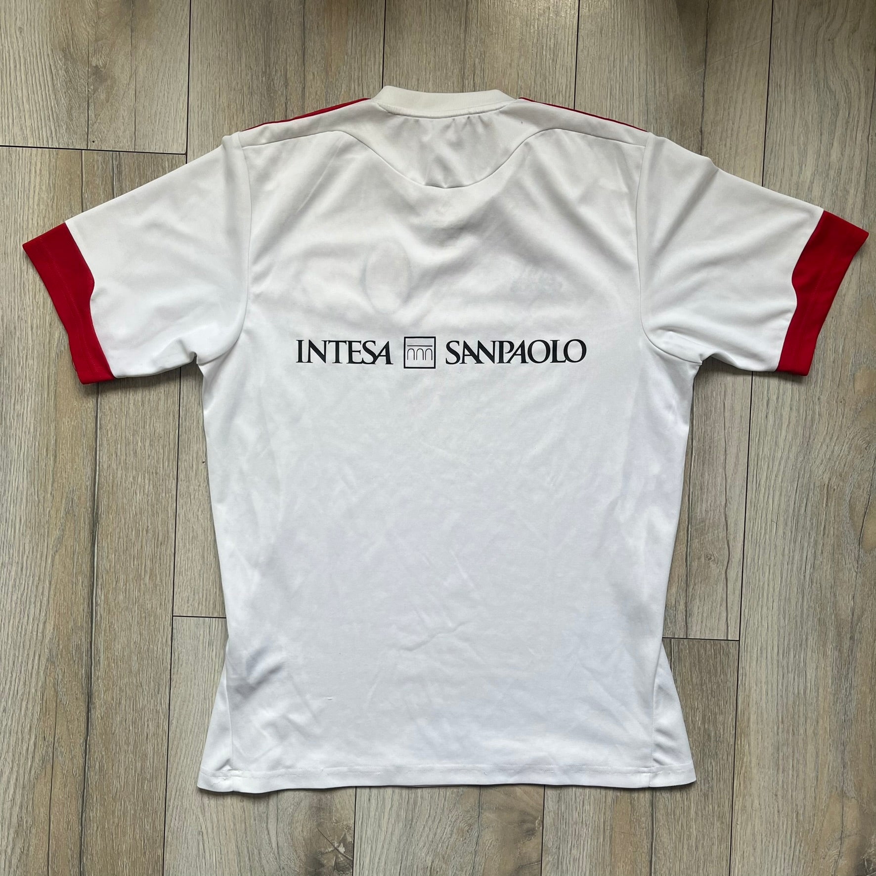 AC Milan x Dolce &amp; Gabbana 2009/10 Training Tee is a white football shirt with red ended short sleeves. The chest features AC Milan and Adidas logos on the sides, and a D&amp;G Dolce &amp; Gabbana Junior logo in the center. Made with Climalite technology, it is designed for performance wear.
