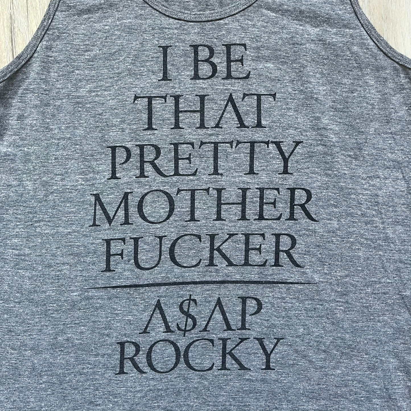 A$AP Rocky 2012 “Peso” Gray Tank Top is a grey sleeveless shirt sold at concerts during the early A$AP Rocky tours. The front features stacked text reading “I be that pretty mother fucker” arranged word-by-word from top to bottom, followed by a line and “ASAP Rocky” beneath. The neckline includes A$AP Rocky branding printed on the tag area.