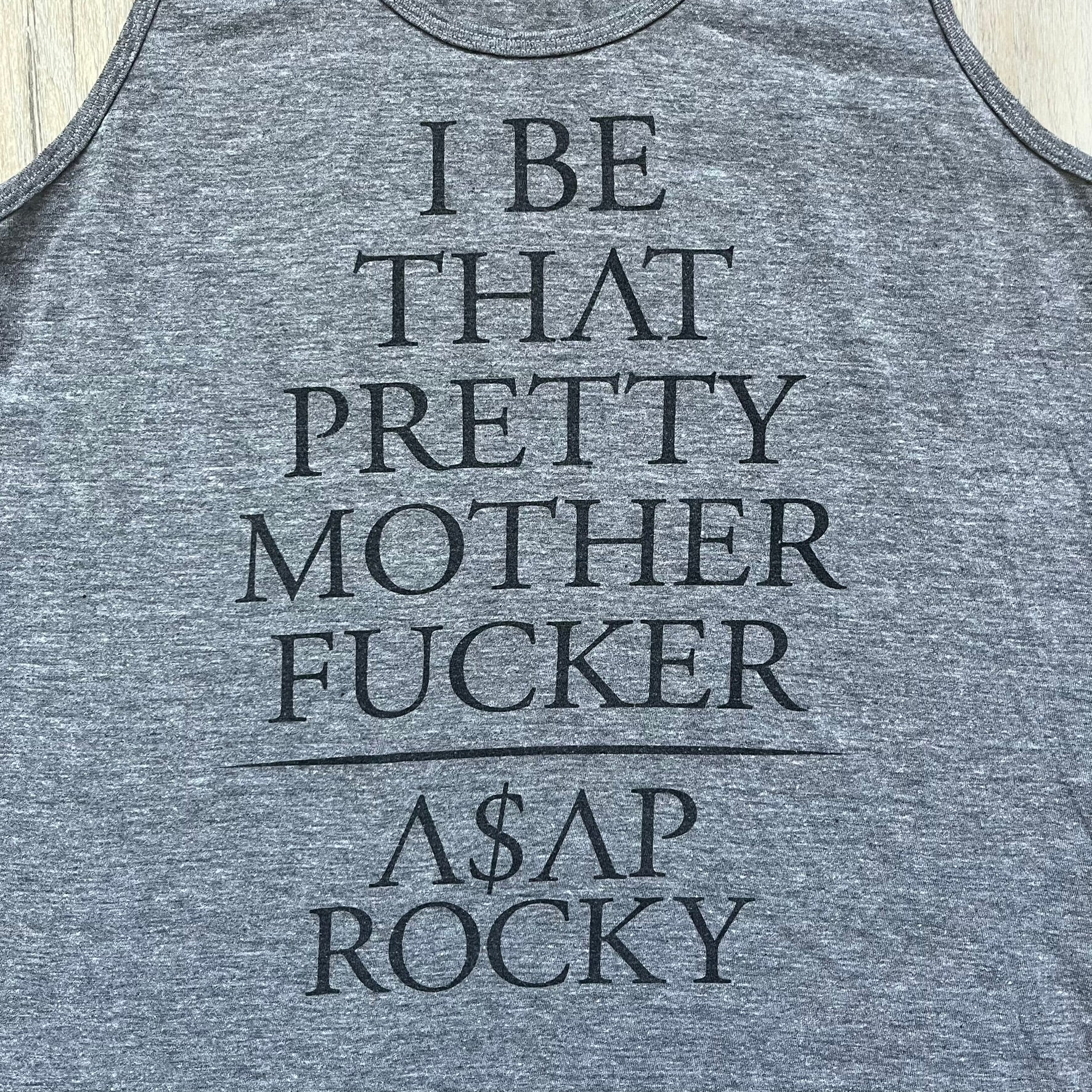 A$AP Rocky 2012 “Peso” Gray Tank Top is a grey sleeveless shirt sold at concerts during the early A$AP Rocky tours. The front features stacked text reading “I be that pretty mother fucker” arranged word-by-word from top to bottom, followed by a line and “ASAP Rocky” beneath. The neckline includes A$AP Rocky branding printed on the tag area.