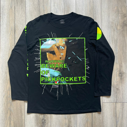 A$AP Rocky 2019 “Injured Generation” Tour “Pickpockets” Longsleeve is a black long-sleeve T-shirt released as part of the Injured Generation tour merchandise collection. The front features a large graphic of A$AP Rocky with green “Warning! Beware of Pickpockets” text. One sleeve includes “1-800-EAT-SHIT” text, while the other features a yellow and green testing-style logo. The back displays large green “Don’t Be a Dummy A$AP Rocky Europe” text layered over a white dummy mask graphic. Made in the USA.