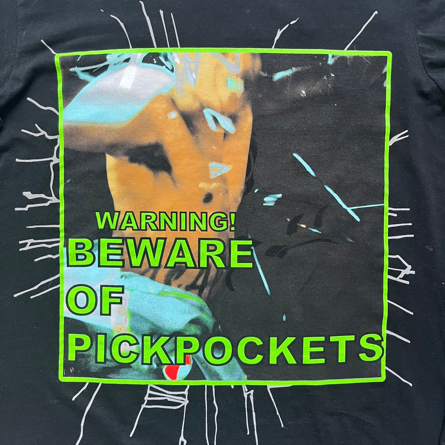 A$AP Rocky 2019 “Injured Generation” Tour “Pickpockets” Longsleeve is a black long-sleeve T-shirt released as part of the Injured Generation tour merchandise collection. The front features a large graphic of A$AP Rocky with green “Warning! Beware of Pickpockets” text. One sleeve includes “1-800-EAT-SHIT” text, while the other features a yellow and green testing-style logo. The back displays large green “Don’t Be a Dummy A$AP Rocky Europe” text layered over a white dummy mask graphic. Made in the USA.