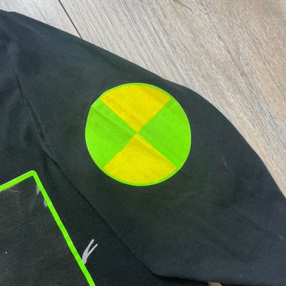 A$AP Rocky 2019 “Injured Generation” Tour “Pickpockets” Longsleeve is a black long-sleeve T-shirt released as part of the Injured Generation tour merchandise collection. The front features a large graphic of A$AP Rocky with green “Warning! Beware of Pickpockets” text. One sleeve includes “1-800-EAT-SHIT” text, while the other features a yellow and green testing-style logo. The back displays large green “Don’t Be a Dummy A$AP Rocky Europe” text layered over a white dummy mask graphic. Made in the USA.